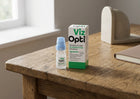 Viz Opti screen eye drops bottle and packaging box placed on a rustic wooden table near a window, with a neutral indoor background.