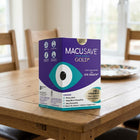 A box of Macusave Gold eye health supplement placed on a wooden dining table in a bright, modern room.