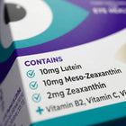 Close-up of a product box showing the 'CONTAINS' label with text listing 10mg Lutein, 10mg Meso-Zeaxanthin, 2mg Zeaxanthin, and Vitamin B2, Vitamin C, on a white background with purple and teal graphics.