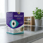 A box of Macusave Gold+ eye healthy food supplement standing on a kitchen countertop with a blurred kitchen background including a plant and stove.