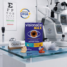 Visionace MAX supplement packaging displayed on a glass tabletop in an optometrist's office, with an eye exam chart, slit lamp, and tonometer in the background.