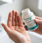 A person holds an open white bottle labeled Ocular Express Glaucomide next to their open palm, which contains a single clear capsule, against a bright, softly blurred bathroom background.