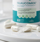 A bottle of Glaucomide dietary supplement capsules with several white capsules and loose white powder scattered on a white surface in the foreground.