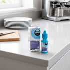 Blink Intensive eye drops bottle and packaging box on a light gray kitchen countertop, with a blurred kitchen background including plates, a cutting board, and a coffee machine.