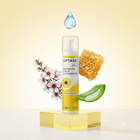 Optase Bio Manuka Oil Eyelid Cleansing Gel bottle displayed on a gold pedestal with floating honeycomb, aloe vera, cherry blossoms, and a water droplet against a soft yellow background.