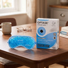 A blue gel cooling mask and its product box by SCOPE OPTASE Cooling Mask Technology are displayed on a wooden table in a cozy, softly-lit room setting.