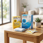 Two Optase product boxes, a folded light blue cloth, and two sachets arranged on a wooden table in a softly blurred living room setting.