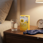 A yellow and white box of Optase Microdial Stimulus Wipes stands on a wooden bedside table next to a glass of water, a blue sleep mask, and an alarm clock in a warmly lit bedroom setting.