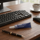 A tube of Hycosan Night hand gel lies on a wooden desk next to a keyboard, mouse, pen, and a cup of coffee.