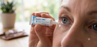 A close-up of a person applying Xailin contact lens gel from a white tube to their eye, with a blurred indoor background.