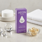 A box of Aeon Repair after eye surgery eye drops stands on a light marble surface, surrounded by skincare props including cotton pads, clear glass spheres, and a small bowl of golden softgel capsules. The box is purple with white text.