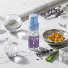 A small bottle of Aeon Repair serum with a lavender label and light blue cap sits on a white marble surface, styled with clear glass spheres, lavender sprigs, a small dish of golden softgel capsules, and an aloe vera slice.