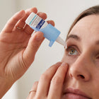 A close-up of a woman applying ARPELEX tear drops from a small blue and white dropper bottle to her eye, with her other hand gently holding her eyelid.