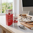 Hycosan Extra eye drops packaging and bottle displayed on a desk next to eyeglasses, a notebook, and a watch in a bright office setting.