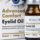 A close-up of an amber glass vial of eyelid oil next to its white and gold retail box. The packaging features a graphic of a blue eye and the brand name 'theeyedoctor+'.