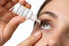 A close-up of a person applying eye drops from an EcoTears bottle to their eye, with the dropper tip touching the tear film. The person's hand and face are visible against a clean white background.