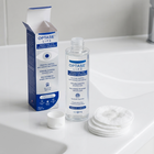 OPTASE LIFE Sensitive Eye Makeup Remover shown with its blue and white retail box, an open clear bottle with white cap, a small white cap, and cotton pads on a white sink counter.