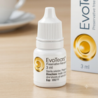A 3 ml bottle of EvoTears Preservative-Free eye drops stands on a light wooden surface next to its product box. The bottle is white with a ribbed cap and features a gold circular logo, while the box in the background is white with black text and a gold circle.
