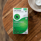 A box of Optase Tea Tree Oil Eyelid Wipes sits on a round wooden table, with a small white candle in a white ceramic dish partially visible in the upper right.
