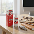 Hycosan Extra eye drops bottle and packaging box displayed on a wooden desk next to eyeglasses, a notebook, and a watch.