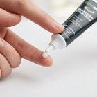 A close-up of a hand squeezing a tube of Optima Manuka 100% Healing Cream, with a small dollop of the white cream resting on another finger against a clean white background.