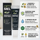 OptiMel Manuka + Eyelid Cream shown with its black outer box and matching squeeze tube, alongside a white informational callout panel detailing key ingredients and benefits including manuka and jojoba oil, everyday skin protection, dryness relief, and honey enrichment.
