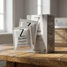 Zocular ZocuWipe eye wipes shown with three individual packet packs and a white product box on a rustic wooden table, with a softly blurred window background.