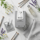 Zocular ZocuWipe eyelash and eye makeup remover wipes arranged on a white marble surface with lavender sprigs, makeup brushes, a glass dropper bottle, and a folded gray cloth.