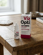 Viz Opti intermediate dry eyes eye drops bottle and packaging box displayed on a rustic wooden table in a warm, softly lit indoor setting.
