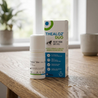 Thealoz Duo relief from dry eyes drops shown with its white bottle and retail box on a wooden table in a softly blurred indoor setting.