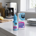 A bottle and box of Blink Intensive Plus liquid gel eye drops are displayed on a kitchen countertop with a blurred coffee maker and plates in the background.