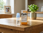 Viz Opti preservative-free brightened eye drops shown with its white and orange box on a wooden table in a bright, modern room.