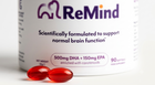 A close-up of a white ReMind supplement bottle with two red softgels placed in front on a clean white background.