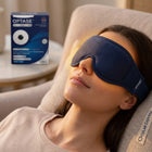 A woman reclining in a beige lounge chair wearing a navy blue Optase sleep mask, with the Optase product box visible on a side table in the background.