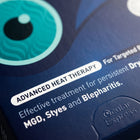 Close-up of a dark blue product box with teal and white text reading 'ADVANCED HEAT THERAPY' and 'Ocular Express'.