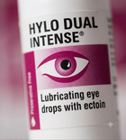 Close-up of a white bottle label for HYLO DUAL INTENSE Lubricating eye drops with ectoin, featuring a magenta eye graphic and pink accent block.