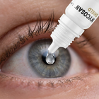 A close-up of a human eye with a dropper bottle labeled HYCOSAN SHIELD applying liquid directly onto the eye, showing a clear drop hanging above the pupil.