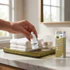 A hand holds a small white bottle labeled HYCOSAN SHIELD over a bathroom counter setup with folded white towels, a gold tray, a jar, and a HYCOSAN Shield box in a bright, modern bathroom setting.