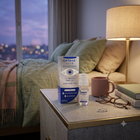 Optase Life Bright Eyes eye drops in a bedroom setting, displayed on a bedside table next to a lamp, glasses, and a mug.