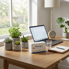A VitroCap Nl medical product box sits on a wooden desk in a bright, modern home office setting, surrounded by potted plants, an open laptop, a lamp, and a notebook.