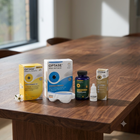 Optase and Hyosan eye care products arranged on a wooden table, including a yellow Optase box, a blue-and-white Optase night mask box, a white protective shield, a dark bottle, and a small white dropper bottle with a Hyosan box in the background.