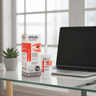 Hylo-Forte preservative-free eye drops shown with its retail box and dropper bottle on a glass tabletop, with a laptop and small potted plant in a bright indoor setting.