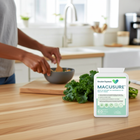 Person preparing food in a kitchen with a bottle of Macusure supplement on the counter.