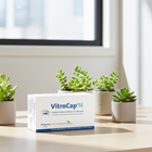 VitroCap'N eye supplement box displayed on a light wooden table in a bright room, surrounded by small potted succulents.